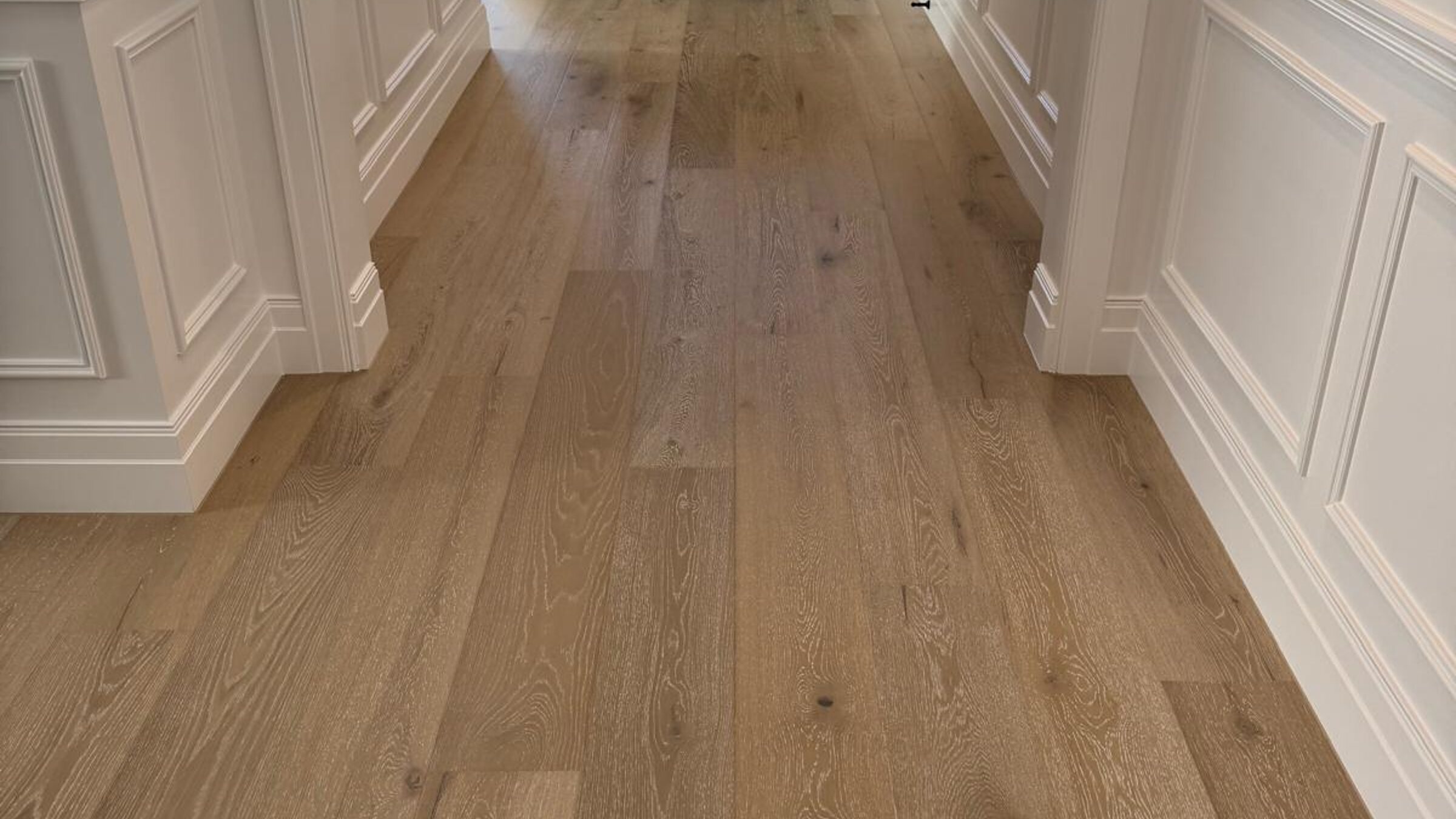 Engineered oak flooring in an entry hallway with wainscoting and a black front door